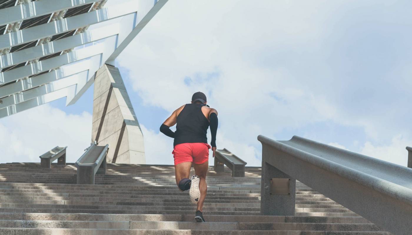 Muscular hispanic Young male dark-skinned athlete running up a flight of stairs with speed, sporty young man in black t-shirt training or working out outdoors while jogging up the steps. Rear view.